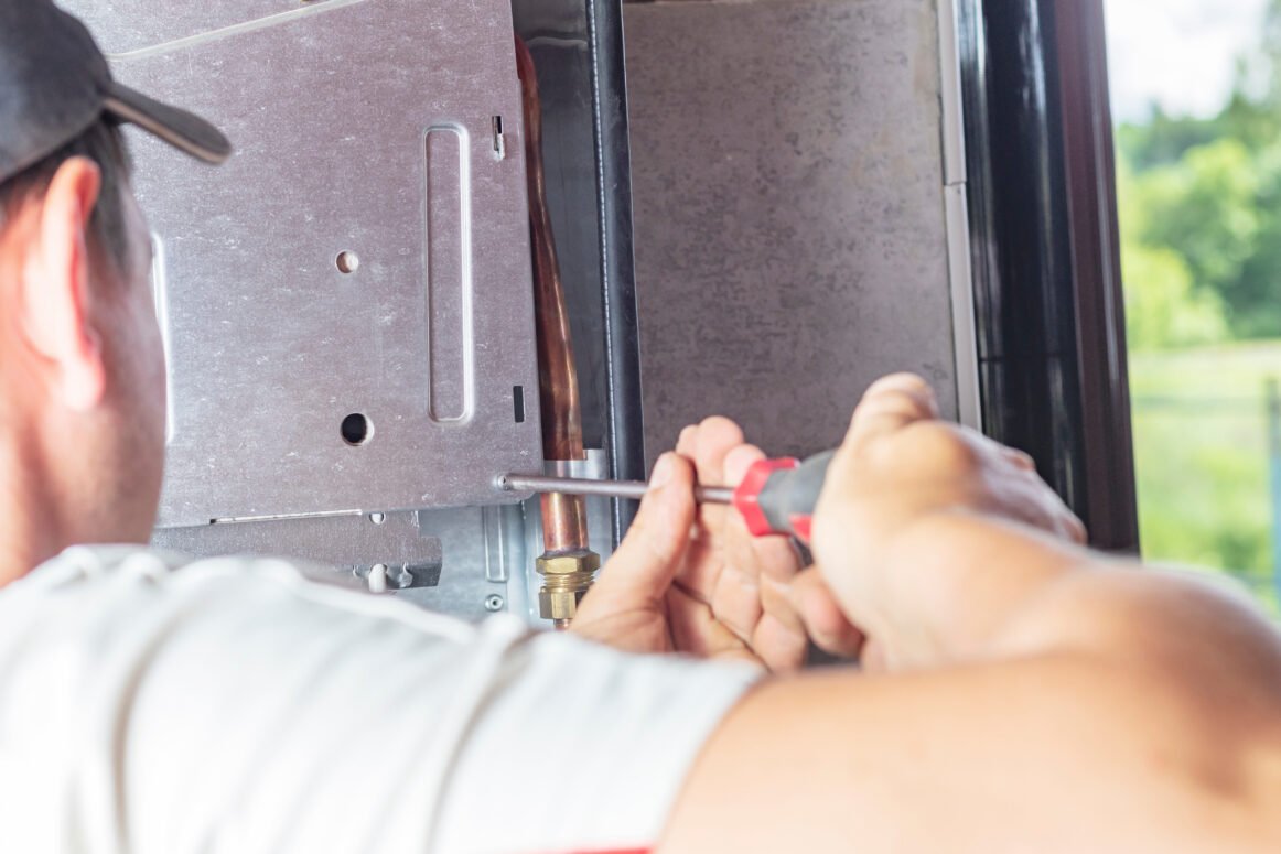 The master sets up a gas boiler, which weighs on the wall. The front dashboard is open. The removal and installation of gas nozzles for gas supply.